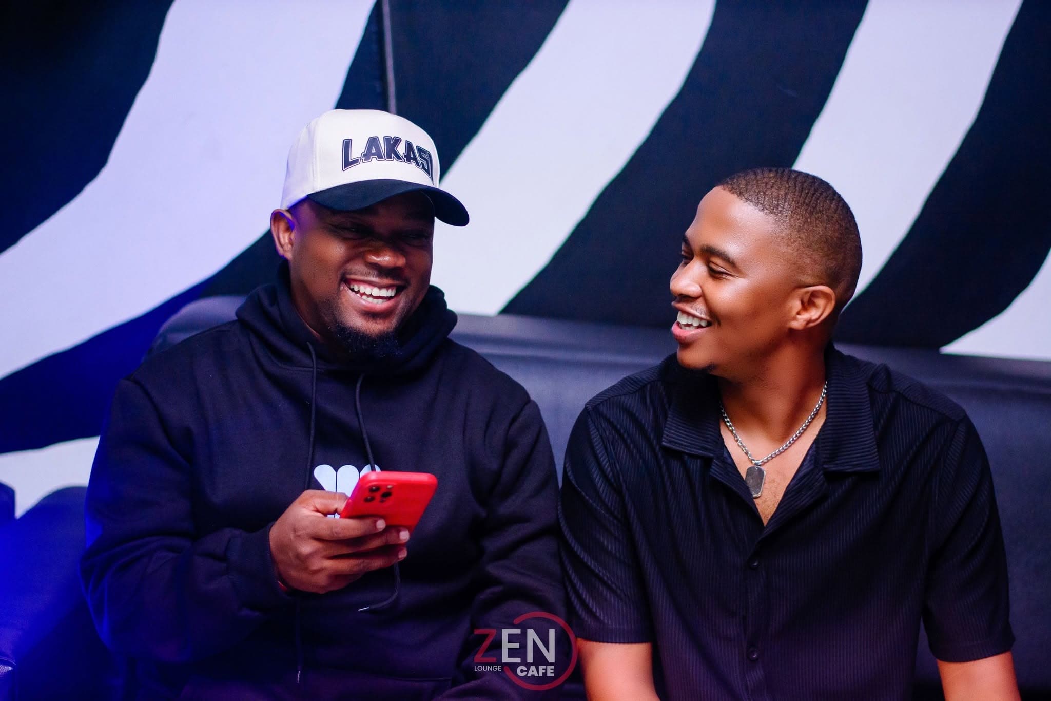 Two friends share a laugh on the lounge seating in front of the zebra-print wall.