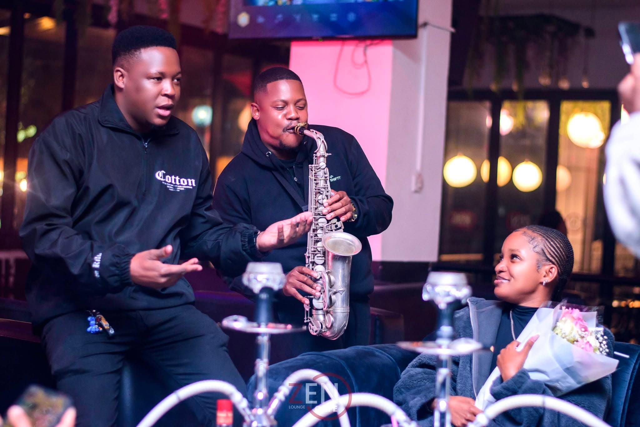 A live saxophonist performs beside celebrating guests, flowers and hookah in view, capturing Zen's evening energy.