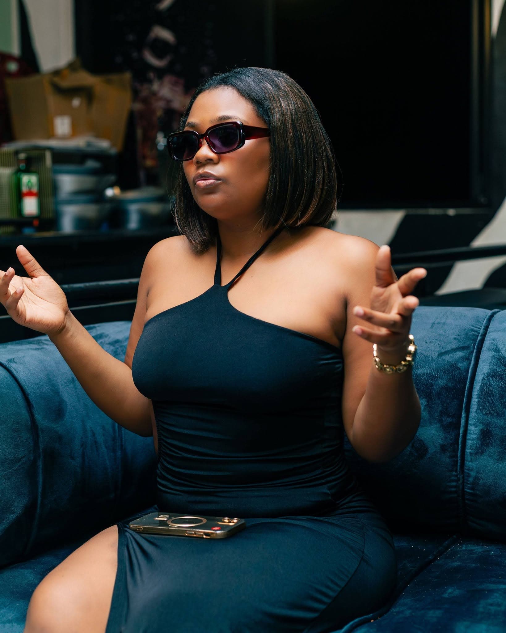 A guest gestures mid-conversation from a blue velvet booth, sunglasses catching the light.